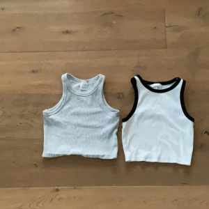 Två ribbade linnetoppar från Zara och H&M - Säljer två snygga ribbade linnetoppar. En ljusgrå från Zara och en vit med svarta kanter från H&M. Båda är ärmlösa och har en sportig look, perfekta till sommaren.