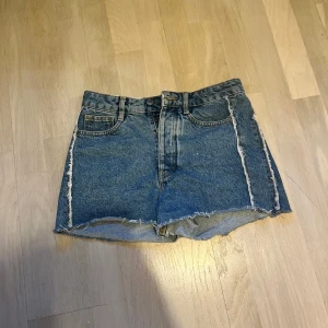 Blå jeansshorts från HM - Säljer ett par klassiska blå jeansshorts med hög midja och råa, fransiga kanter. Shortsen har fem fickor, bälteshällor och stängs med knapp och dragkedja. Perfekta för sommaren och ger en avslappnad vibe. Pris kan diskuteras!💕