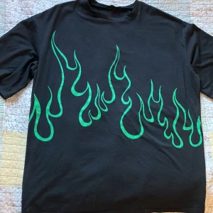 Svart t-shirt med grönt flamor - Cool svart t-shirt från SHEIN🥲 Jag köpte den på plick så den är begagnad. T-shirten är lite nopprig? ..  oversized passform? Perfekt för dig som vill sticka ut med en edgy stil.😎