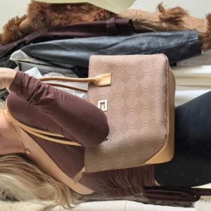 Brun axelväska  - Säljer denna super snygga hård strukturerade väskan med ett G på. Köpt secondhand! Super fin och klassisk. Har små tecken på slitage vid en brun ram men annars super gott skick. Väskan har dragkedja upptill och två långa handtag. Perfekt storlek för vardagens alla prylar och har ett stilrent metallogo framtill.