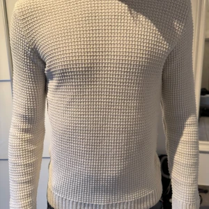 Beige stickad tröja med strukturmönster - Säljer en beige stickad tröja med lång ärm och snyggt strukturmönster. Tröjan har ribbade muddar vid ärmslut och nederkant. Perfekt för lager-på-lager och passar till jeans eller chinos.