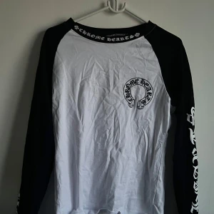 Chrome Hearts långärmad tröja med tryck - Säljer en långärmad svartvit tröja från Chrome Hearts med stora tryck på både fram- och baksida samt längs ärmarna. Tröjan har svart krage och ärmar, och vit framsida och rygg. Perfekt för dig som gillar streetwear och tydliga loggor.