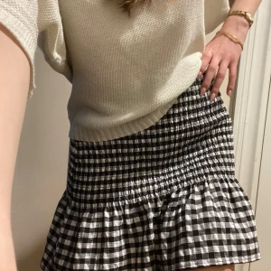 Svartvit rutig kjol med volang - Supersöt svartvit rutig kjol med smock i midjan och volang nertill. Perfekt för dig som gillar en lekfull och trendig stil. Kjolen är kort och har en bekväm passform som passar till många olika outfits.