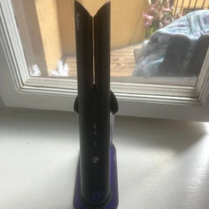 Dyson svart trådlös plattång med laddningsställ - Säljer en svart plattång från Dyson med lila detaljer. Plattången står på ett matchande laddningsställ och har keramiska plattor. Perfekt för att styla håret med slät finish. Sladdlös design för enkel användning. Mycket bra skick, använder inte längre så därför säljer jag. Man får med plattången, laddaren och laddningsstället. Den är mycket bra kvalitet och håret blir silkeslent och platt.