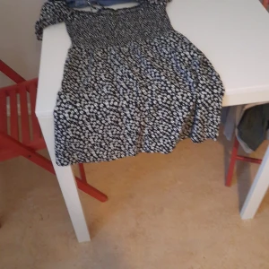 Svart blommig kortklänning med puffärm - Supersöt svart kortklänning med vitt blommönster och puffiga korta ärmar. Klänningen har en smockad överdel och utställd kjol, perfekt för sommarens alla tillfällen. Bekväm och luftig passform.