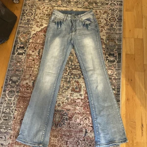 Ljusblå bootcut jeans - Säljer ett par ljusblå bootcut jeans med klassisk femficksdesign och lätt slitna detaljer vid fickorna. Jeansen har normal passform och är tillverkade i denim. Perfekta för dig som gillar en retroinspirerad look.