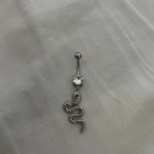 Navelpiercing med orm och sten - Snygg navelpiercing i titan med en glittrande sten och en hängande orm. Perfekt accessoar för dig som vill sticka ut med ett unikt smycke. Köpt för 200 och endast använd en gång💞