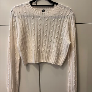 Kabelstickad croptop - Säljer en cremevit, stickad, tunn croptop med långa ärmar. Köpt på HM för ett par år sedan men tyvärr inte använd så mycket. Perfekt en kylig sommarkväll eller över ett linne eller liknande. Storlek M.