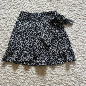 Blommig kjol - Säljer en jättesnygg kjol som passar perfekt nu till sommaren. Den har ett vitt blommigt mönster med volang och en söt rosett på sidan. Dragkedjan kan vara lite trög. 💗KOLLA CAPTION