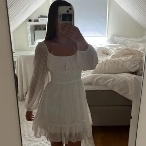 Vit kortklänning - Supervacker vit kortklänning med diskreta prickar och volangdetaljer. Klänningen har långärmade, lätt puffiga ärmar och markerad midja. Perfekt för skolavslutning och sommarens alla tillfällen! Söt och luftig modell med romantisk känsla. Så skön på! Använd en gång på skolavslutningen. Dragkedja på sidan.