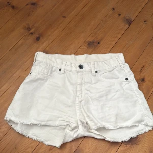 Vita jeansshorts från Dr Denim - Säljer ett par vita jeansshorts från Dr Denim med råa kanter och klassisk femficksdesign. Shortsen har knapp och dragkedja framtill samt bälteshällor. Perfekta för varma dagar och enkel att matcha med olika toppar.