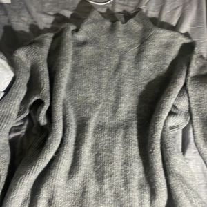 Grå stickad polotröja från 157 - Mysig grå stickad polotröja från 157 med hög krage. Perfekt för kyliga dagar och enkel att matcha med olika outfits. Tröjan har lång ärm och en klassisk, rak passform.