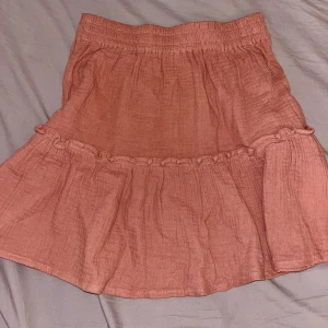 Rosa/peach volangkjol  - Söt, kort, rosa kjol med volangdetalj och resår i midjan. Kjolen är gjord i ett tunt, luftigt tyg och har en avslappnad passform. 