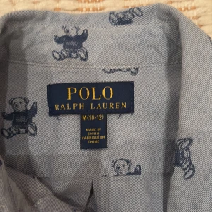 Blå skjorta med björnmönster från Polo Ralph Lauren - Säljer en blå skjorta från Polo Ralph Lauren med långa ärmar och knappar framtill. Skjortan har ett lekfullt mönster med små björnar och en broderad logga på bröstet. Perfekt för dig som gillar grisch stil  