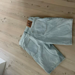 Ljusblå jeansshorts från Sweet Skibs - Säljer ett par ljusblå jeansshorts från Sweet Skibs. Klassisk femficksmodell med gylf och knapp framtill samt läderpatch med logga bak. Perfekta för varma dagar och enkel att matcha med olika toppar.