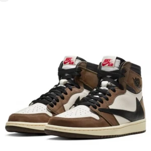 Nike Air Jordan 1 Travis Scott - Säljer ett par Nike Air Jordan 1 Travis Scott med bruna, vita och svarta paneler. Skorna har klassisk hög siluett, svart swoosh och snörning framtill. Perfekta för dig som vill sticka ut med en ikonisk sneaker.