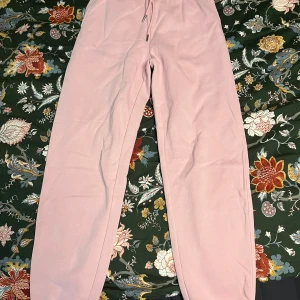 Ljusrosa mjukisbyxor från H&M - Säljer ett par ljusrosa mjukisbyxor från H&M i storlek XS. Byxorna har resår i midjan med dragsko och raka ben. Perfekta för en avslappnad stil och riktigt sköna att ha på sig.