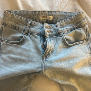 Pull & bear Ljusblå bootcut jeans - Säljer ett par super trendiga  ljusblå jeansbyxor med bootcut passform och låg midja. Klassisk femficksmodell med knapp och dragkedja framtill. Perfekta för en avslappnad och trendig look. Säljer då dem ej passar!