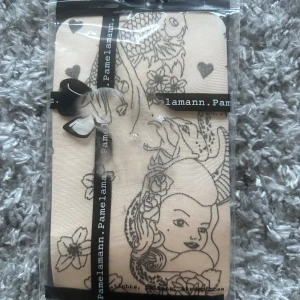 Beige strumpor med tatueringsmönster från Pamela Mann. I onesize - Säljer ett par beige strumpor från Pamela Mann med svart tatueringsinspirerat mönster som föreställer en kvinna, blommor och hjärtan. Strumporna är tunna och har en unik design som sticker ut. Helt nya i onesize