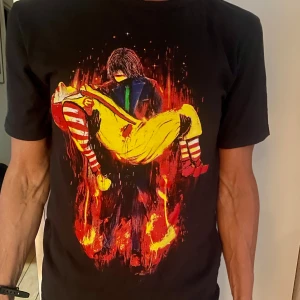 Svart t-shirt med unikt Mickal Jackson tryck - Svart t-shirt med Michael Jackson som bär en döende Ronald McDonald  T-shirten har rund hals och korta ärmar. Perfekt för dig som gillar unika och uttrycksfulla motiv.