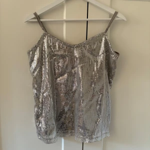 Silvrigt paljettlinne - Paljettlinne i silver från Vero Moda, perfekt till fest! Storlek M men skulle även säga att den passar även S, och eventuellt XS eller L också eftersom längden på axelbanden går att justera! Har endast använt den en gång så som ny i skicket🌟
