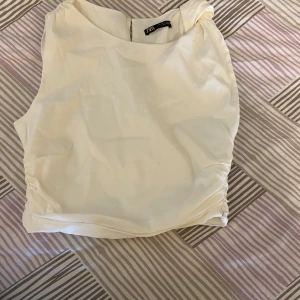 Vit ärmlös topp från Zara - Säljer en stilren vit ärmlös topp från Zara. Toppen har en enkel och clean design med lätt rynkade sidor och rund halsringning. Perfekt att matcha med både jeans och kjol.