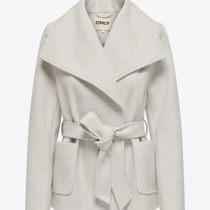 Ljusgrå kappa med bälte från ONLY - Snygg beige kappa från ONLY med bred krage och knytskärp i midjan. Jackan har stora fickor framtill och en elegant, stilren design som passar perfekt till många outfits. Ny pris 700kr om jag minns rätt 🥰Köpt i butik i västerås, den är använd så den är nopprig och ena fickan har börjat låssna lite. 