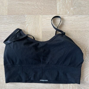 Svart ribbad sport-bh  - En svart ribbad linnetopp med smala axelband och croppad passform. Perfekt att styla med höga jeans eller kjol för en enkel och clean look. Mjuk och stretchig för maximal komfort.