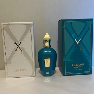 Xerjoff Erba Pura Eau de Parfum 100ml - Lyxig parfym från Xerjoff, Erba Pura, i en stilren blå flaska med gulddetaljer och spetsig guldfärgad kork. Kommer i exklusiv förpackning med färgglad insida. Flaskan rymmer 100 ml och har en modern, geometrisk form.