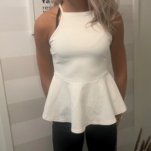 Vit peplum linne med halterneck - Säljer en vit linne-topp med peplumskärning och halterneck. Toppen är ärmlös och har en snygg, figurnära passform upptill som släpper ut i en volang nertill. Perfekt för dig som gillar stilrena och fräscha plagg till sommaren.