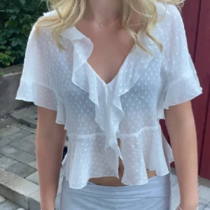 Vit volangblus från Zara - Superfin vit blus från Zara med volanger och prickigt mönster. Blusen är genomskinlig, har v-ringning och korta ärmar med volangdetaljer. Perfekt för sommardagar och ger en romantisk vibe till outfiten.