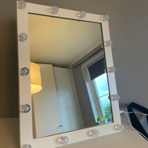 Sminkspegel med LED-lampor - Snygg sminkspegel med vit ram och inbyggda LED-lampor runt hela spegeln. Perfekt för att få till den där flawless makeup-looken med bra belysning. Spegeln står stadigt på bordet och kopplas in med sladd. Ger en lyxig känsla till sminkhörnan. 
