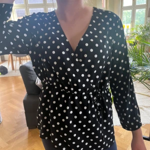 Svart prickig omlottblus med knyt - Svart omlottblus med vita prickar och v-ringning. Blusen har halvånga ärmar och knyt i midjan så den sitter lite bättre och man kan spänna den lite som man vill. Tunt och lätt material som känns skönt mot huden. 💓💓🥰🥰✨