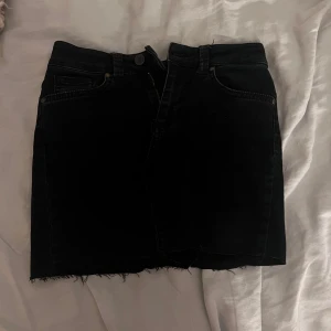 somrig mörkblå jeanskjol OBS KOLLA BIO - KAN SY KJOLEN KORTARE TILL ÖNSKAD LÄNGD!! sy kortare kostar 30 kr till!! Svart jeanskjol från Object med rå kant nertill och klassiska femficksdetaljer. Kjolen är kort och har dragkedja och knapp framtill. Öppen för prisändringar!!