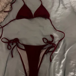Mörkröd bikini med knyt - Snygg mörkröd bikini med klassisk trekants-bh och smala axelband. Underdelen har knyt i sidorna för en justerbar passform. Perfekt för stranden eller poolen. Materialet känns mjukt och stretchigt.