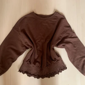 Brun tröja med volang från Stories - Säljer en brun långärmad tröja från Stories i storlek M. Har bara använt den ett fåtal gånger och är därför i bra skick