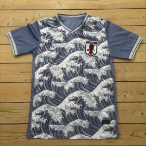 Japan fotbollströja Mitoma #7 Nike - Japan landslagströja med Mitoma #7 på ryggen. Tröjan har ett unikt vågmönster inspirerat av japansk konst, blå och vita färger, V-ringning och korta ärmar. Tillverkad i Dri-Fit-material för bra andningsförmåga. Perfekt för dig som vill sticka ut på planen eller läktaren.