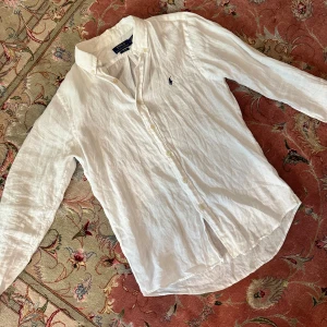 Vit linneskjorta från Polo Ralph Lauren - Säljer en fräsch vit skjorta i linne från Polo Ralph Lauren. Slim fit-modell med klassisk krage, knappar framtill och broderad logga på bröstet. Perfekt för en clean och stilren look. Långärmad och riktigt skön på sommaren.