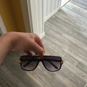 Carrera liknande solglasögon  - Snygga solglasögon med svart, kantig båge och coola guldiga detaljer på sidorna och upptill. Glasen är mörka och har en lätt toning. Perfekt accessoar för att lyfta din stil och ge en lyxig känsla.