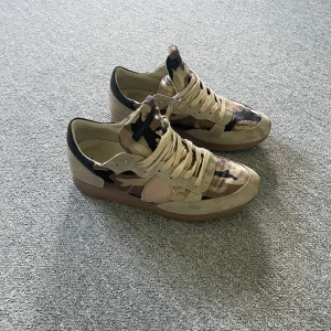 Philippe Model skor - Snygga sneakers från Philippe Model med beige mockadetaljer och camouflagemönster i beige, brunt och svart. Skorna är stl 42. Skriv gärna om du har frågor