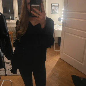 Svart blus med knyt och prickar - Svart blus från H&M med diskret prickigt mönster, v-ringning och knytband vid halsen. Långa ärmar med resår vid ärmslut och lätt volangdetalj upptill. Tunn och luftig, perfekt till jeans eller kjol.