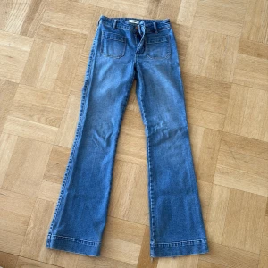 Blå bootcut jeans från Wrangler - Säljer ett par klassiska blå bootcut jeans från Wrangler med hög midja och råa kanter nertill. Jeansen har framfickor, bakfickor med Wrangler-logga och är tillverkade i mjukt denim. 