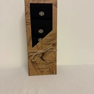 Svarta bambustrumpor från Bambusa - 5-pack svarta klassiska strumpor från Bambusa i unisexmodell. Tillverkade av mjuk och miljövänlig bambuviskos med förstärkt tå och häl. Strumporna har en diskret logga och är sömlösa för extra komfort. Perfekta för dig som gillar stilrena och sköna strumpor.