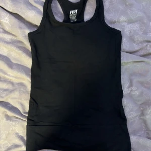 Svart linnetopp från WA Action Sports - En klassisk svart linnetopp från WA Action Sports med brottarrygg. Perfekt för träning eller chill dagar. Tillverkad i mjuk bomull som andas och sitter skönt mot kroppen. Enkel och stilren design utan mönster eller detaljer.