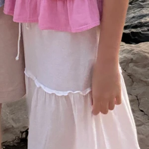 Vit långkjol med volangdetaljer - Superfin vit långkjol med volangdetaljer. Kjolen har en luftig och flowy känsla, perfekt för varma dagar. Man knyter den framtill så den kan passa både S och M.