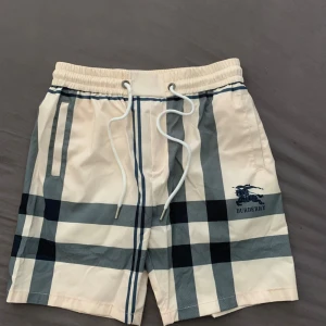 Burberry rutiga badshorts med snörning - Snygga badshorts  i klassiskt  rutigt mönster. Shortsen har elastisk midja med vit snörning och Burberry-logga broderad framtill. Perfekta för sommaren och strandhäng. Helt nya!