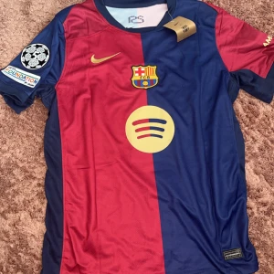 FC Barcelona Lewandowski matchtröja - Snygg FC Barcelona matchtröja med Lewandowski och nummer 9 på ryggen. Tröjan är kortärmad, har klassiska blå och röda fält, gult Nike-märke och klubbmärke på bröstet. Tillverkad i lätt och ventilerande polyester, perfekt för fotboll eller att bära som supporter.