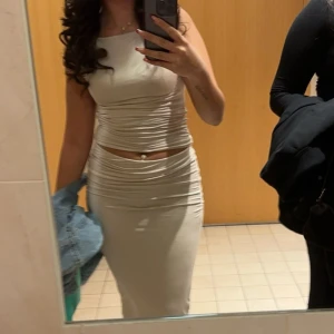 Beige långkjol med matchande topp - Säljer en snygg Beige långkjol med matchande topp. Settet har en tight passform och markerar midjan med en liten cut-out. Perfekt för dig som vill ha en stilren och trendig look.