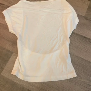 Vit croppad topp med öppen rygg - Snygg vit topp i bomull med korta ärmar och en cool öppen rygg. Modellen är croppad och har en enkel, stilren look som passar perfekt till jeans eller kjol. Perfekt för dig som gillar minimalistisk stil med en twist.