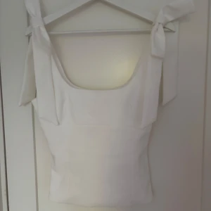 Vit linnetopp med knytband från Zara - Supersöt vit linnetopp från Zara med breda axelband som knyts i stora rosetter. Toppen har en rak, något figurnära passform och är tillverkad i ett slätt tyg. Perfekt för en fräsch och stilren look i sommar.